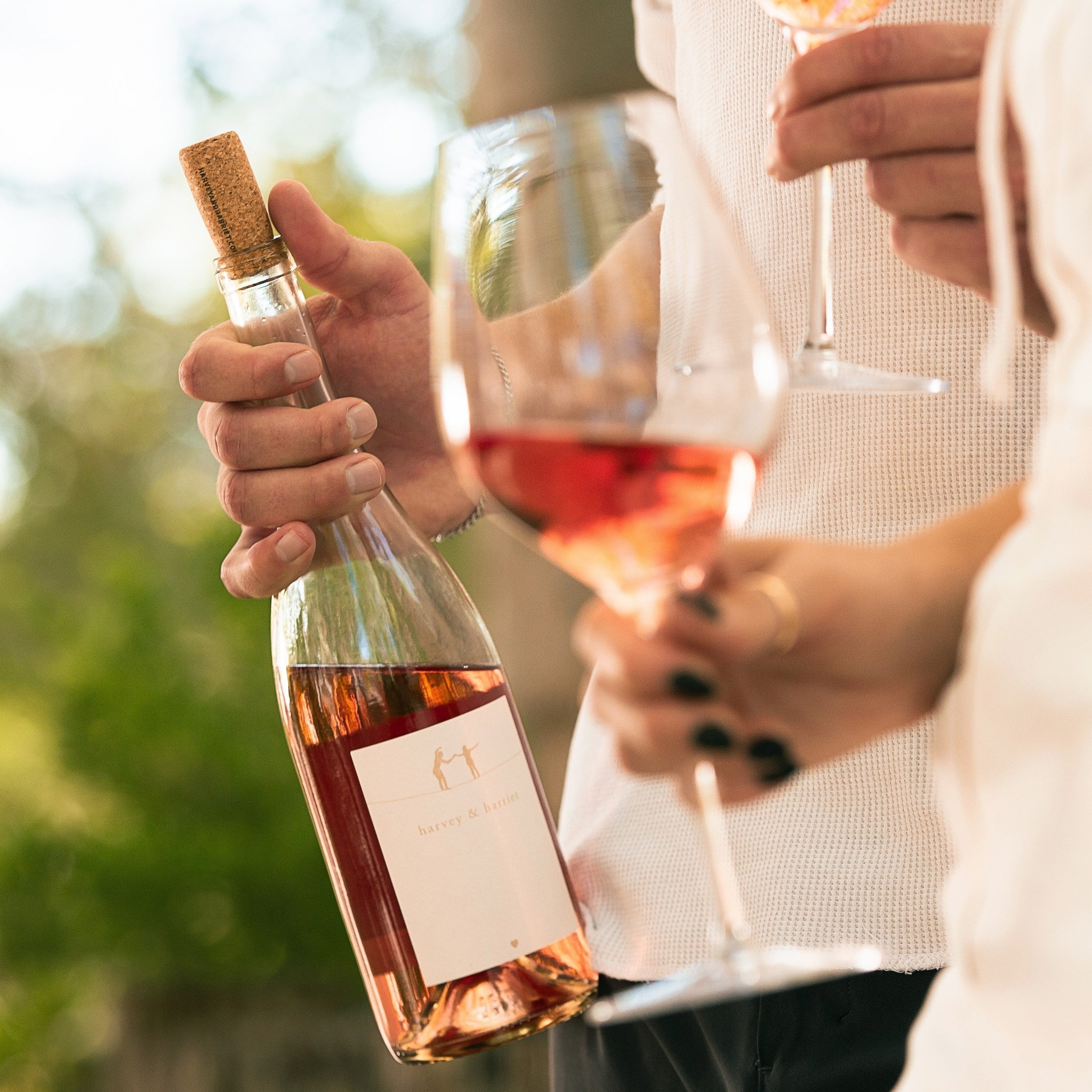 A bottle of 2023 Harvey & Harriet Rose being held by a man with a glass, held by a woman, is in the foreground.