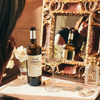 A woman gets ready, putting in an earring while looking in a mirror. A bottle of Double Diamond sauvignon blanc and her glass sit on the vanity. 