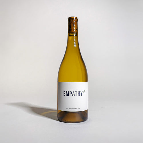 A bottle of 2020 Empathy White Wine, front label facing forward, on a light gray background with a faint shadow being cast to the left side.