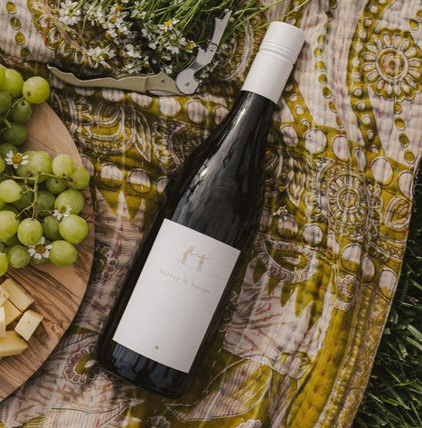 A bottle of 2021 Harvey & Harriet White Blend laying label side up on a quilt with snacks