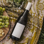 A bottle of 2021 Harvey & Harriet White Blend laying label side up on a quilt with snacks