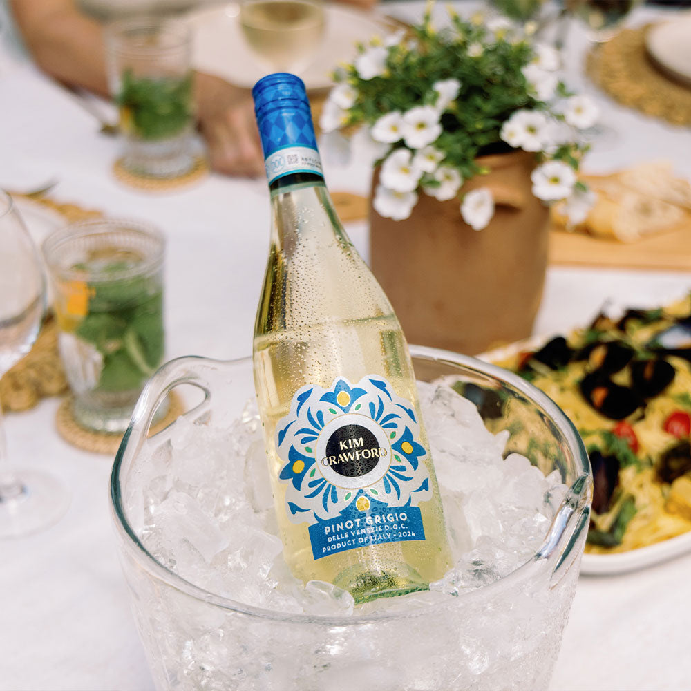 A bottle of Kim Crawford Pino Grigio in a wine bucket surrounded by ice with a blurred background