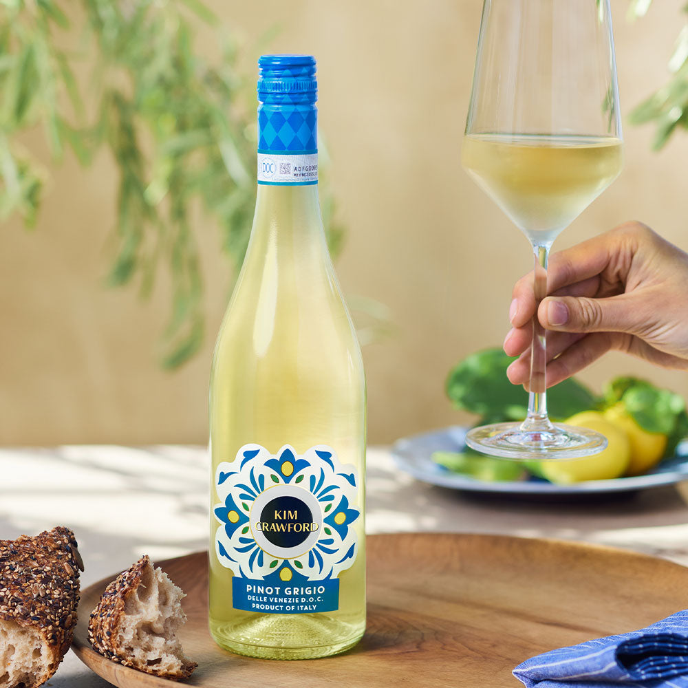 A bottle of Kim Crawford Pino Grigio with a person holding a wine glass 