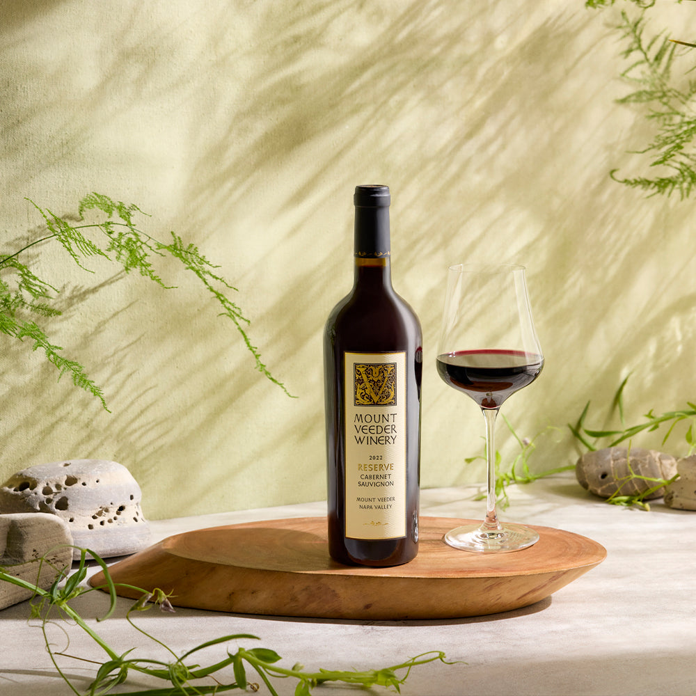 Bottle of Mount Veeder Winery Reserve Cabernet Sauvignon, glass of wine on a wood tray with natural background.