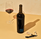 Bottle of Saldo Bavarian Lion Vineyard Petite Sirah on a yellow table with a wine glass and the cork on a corkscrew