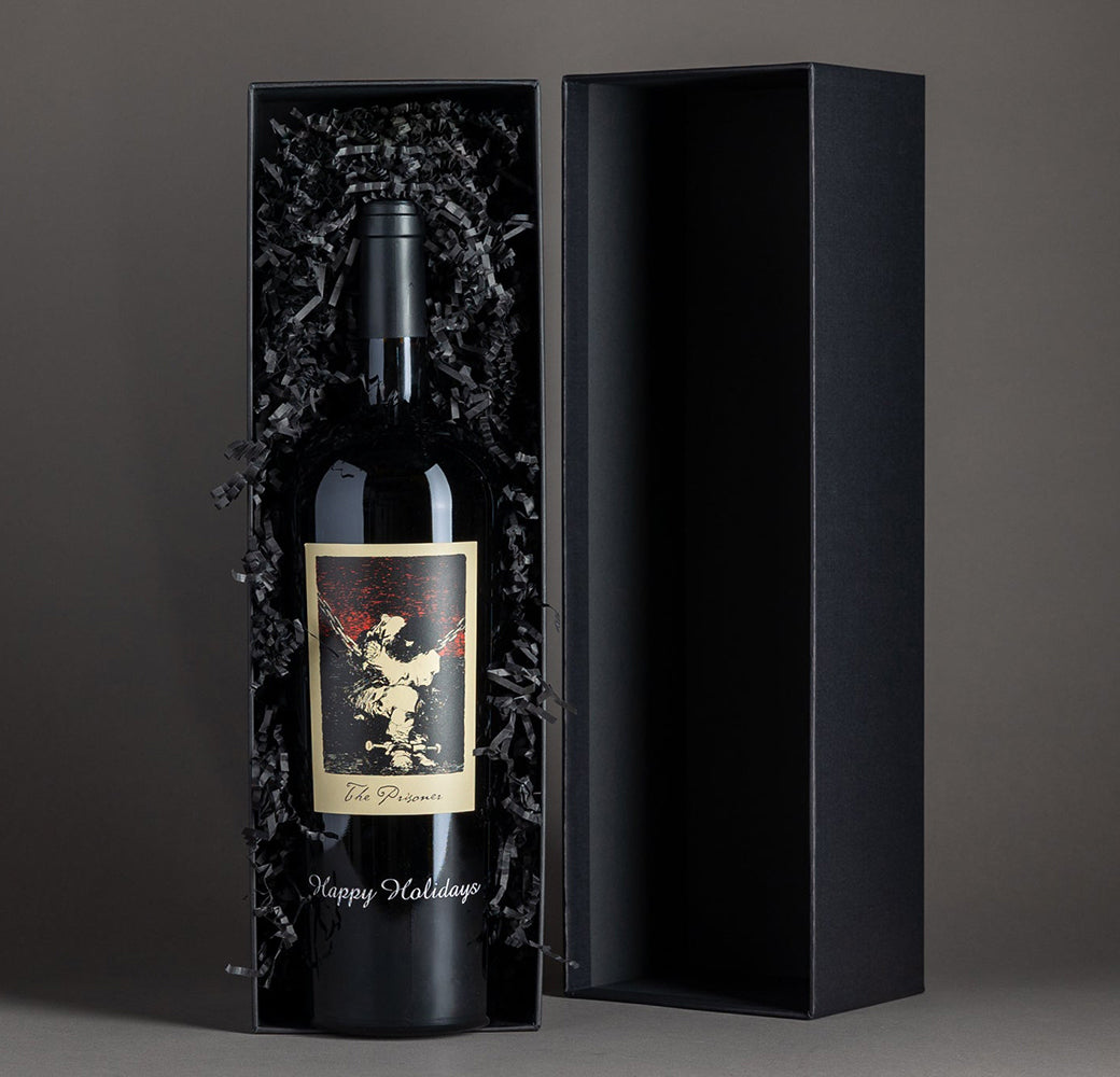 The Prisoner Red Blend etched with "Happy Holidays" in a black gift box on a gray background in the box